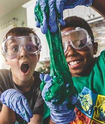 Two boys laugh while playing with sticky green goop during a STEM event.
