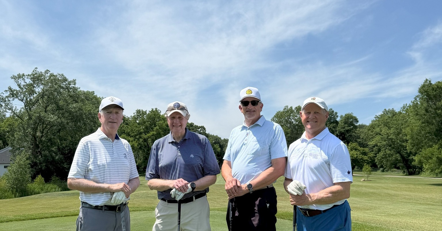 Four men smile at the camera, holding their golf clubs